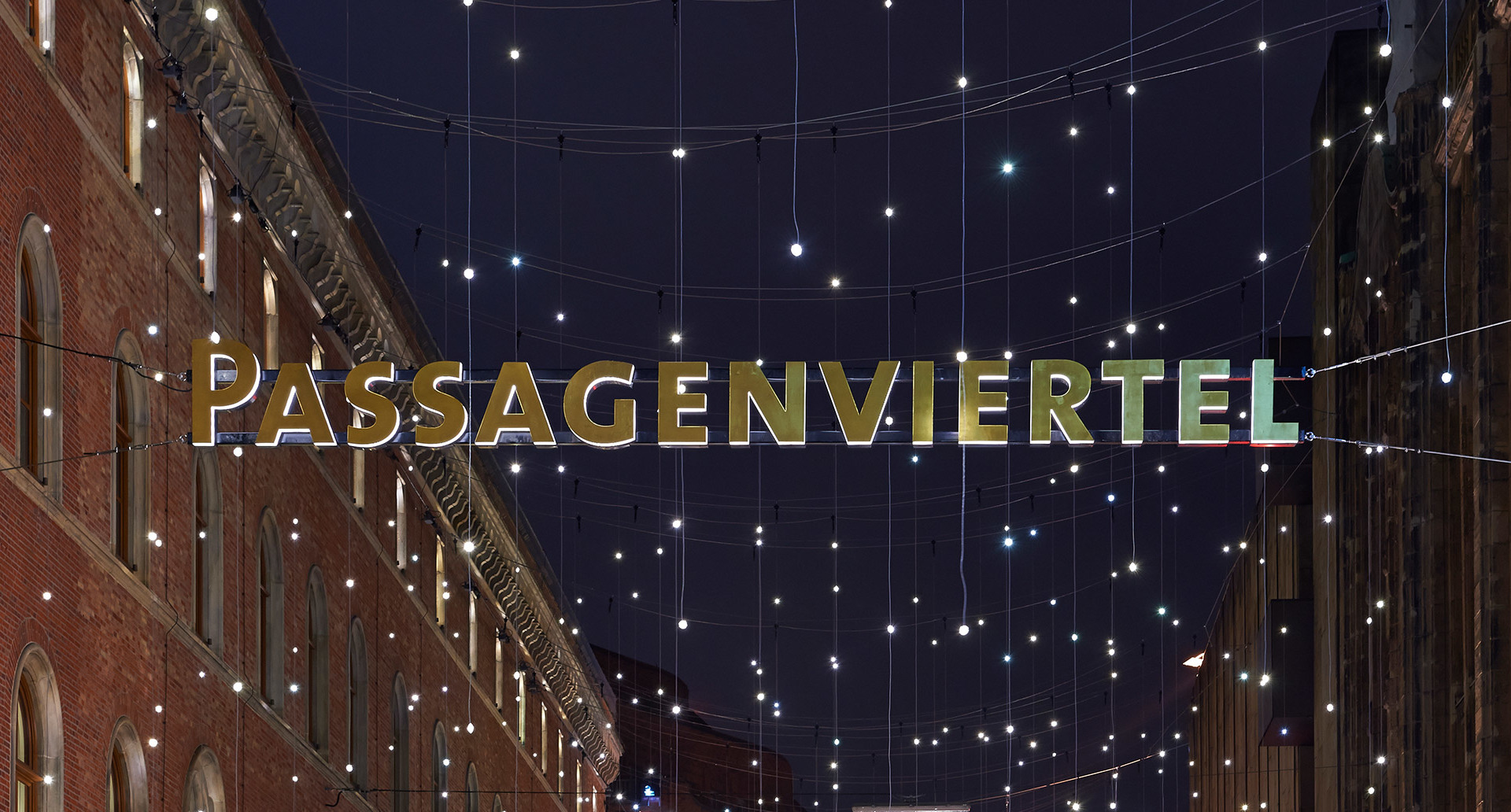 Vista notturna della strada Passagenviertel con insegna illuminata e fili di piccole luci bianche sospesi tra storici edifici in mattoni