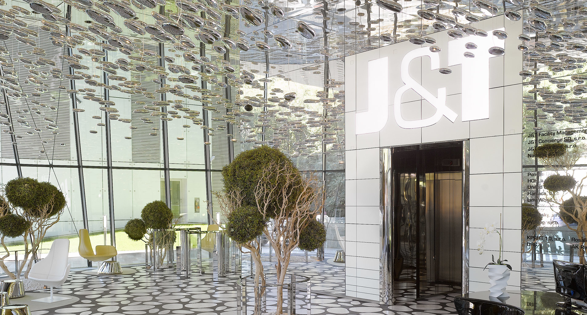 Ingresso moderno con soffitto a specchio con centinaia di piccole luci a sospensione, alberi topiaria e un'entrata con logo J&I.