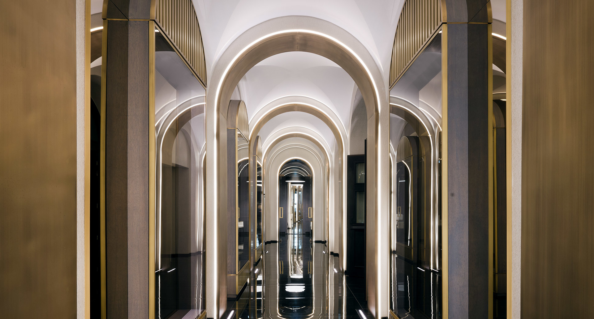 Elegant corridor with repeating illuminated arches, gold trim accents, and integrated linear lighting creating a luxurious perspective effect.
