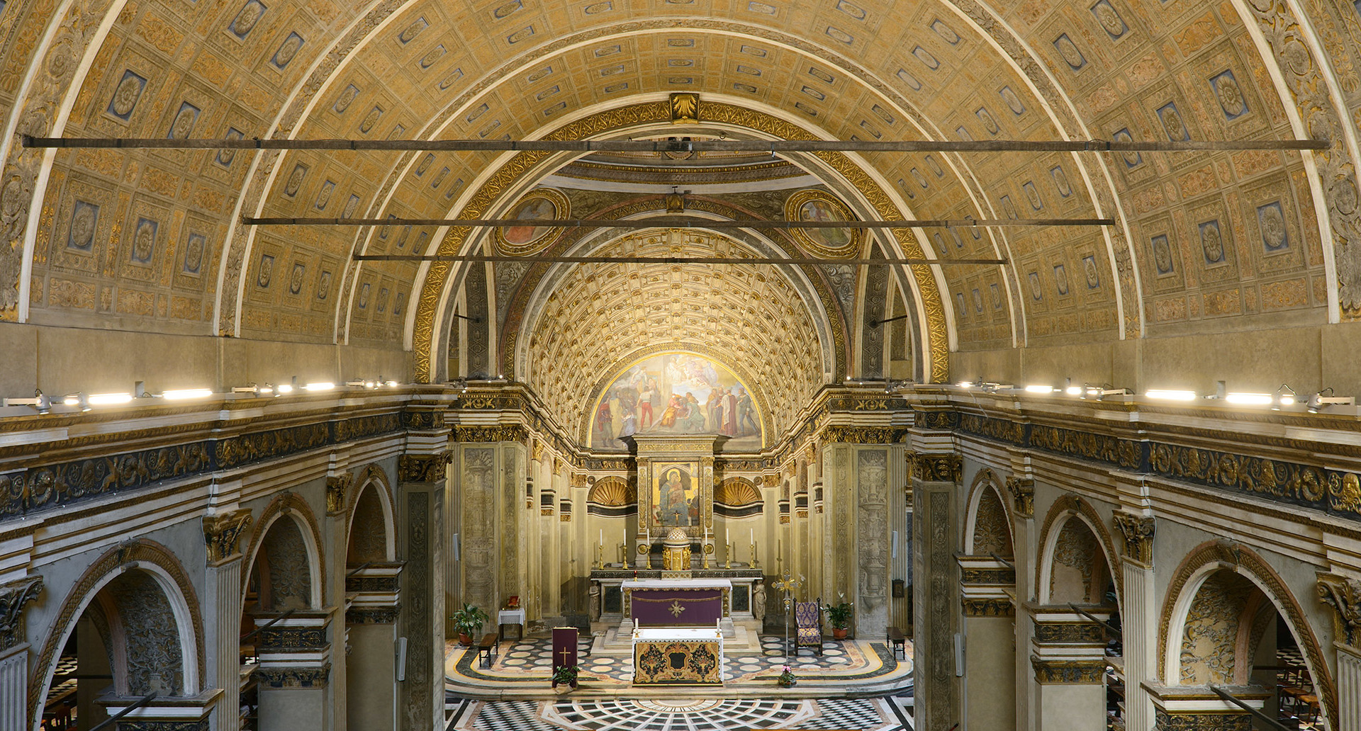Grand church interior with gilded barrel-vaulted ceiling, ornate apse mosaic, marble altar, and linear lighting system along the nave