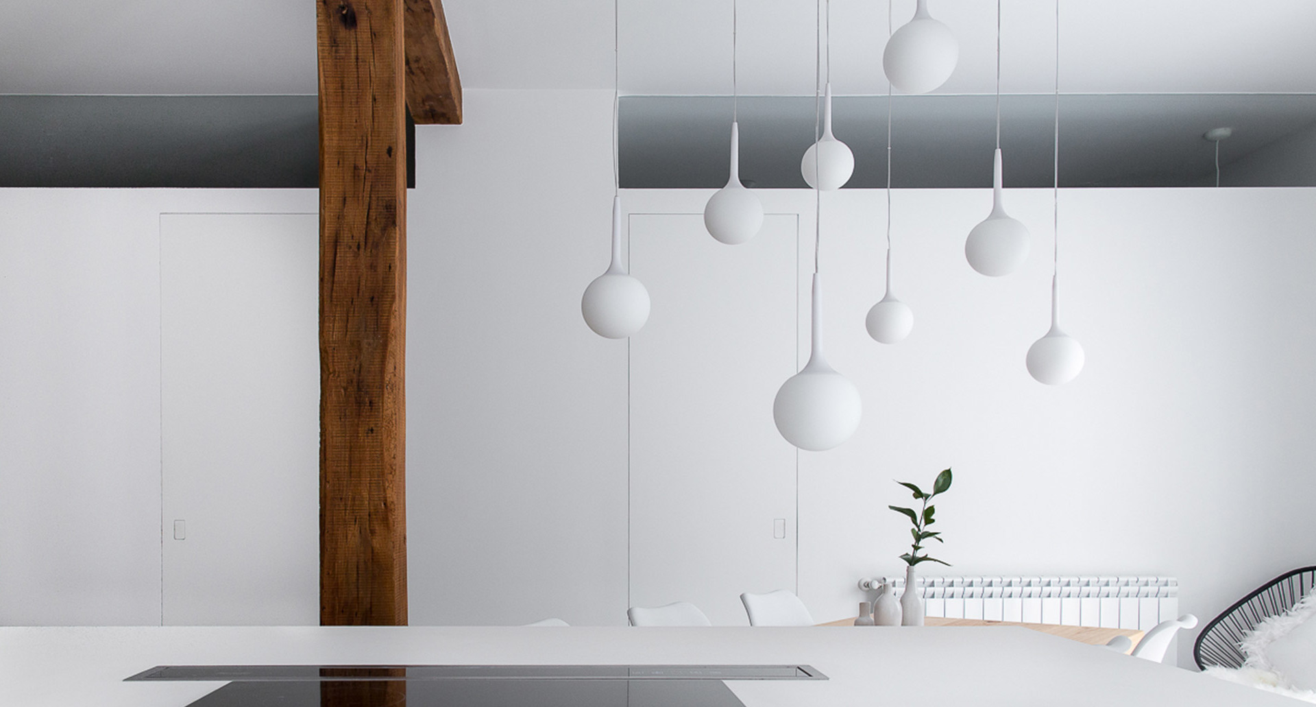 Gruppo di lampade a sospensione bianche con globi sferici e forme a goccia appese a diverse altezze in un interno minimalista bianco