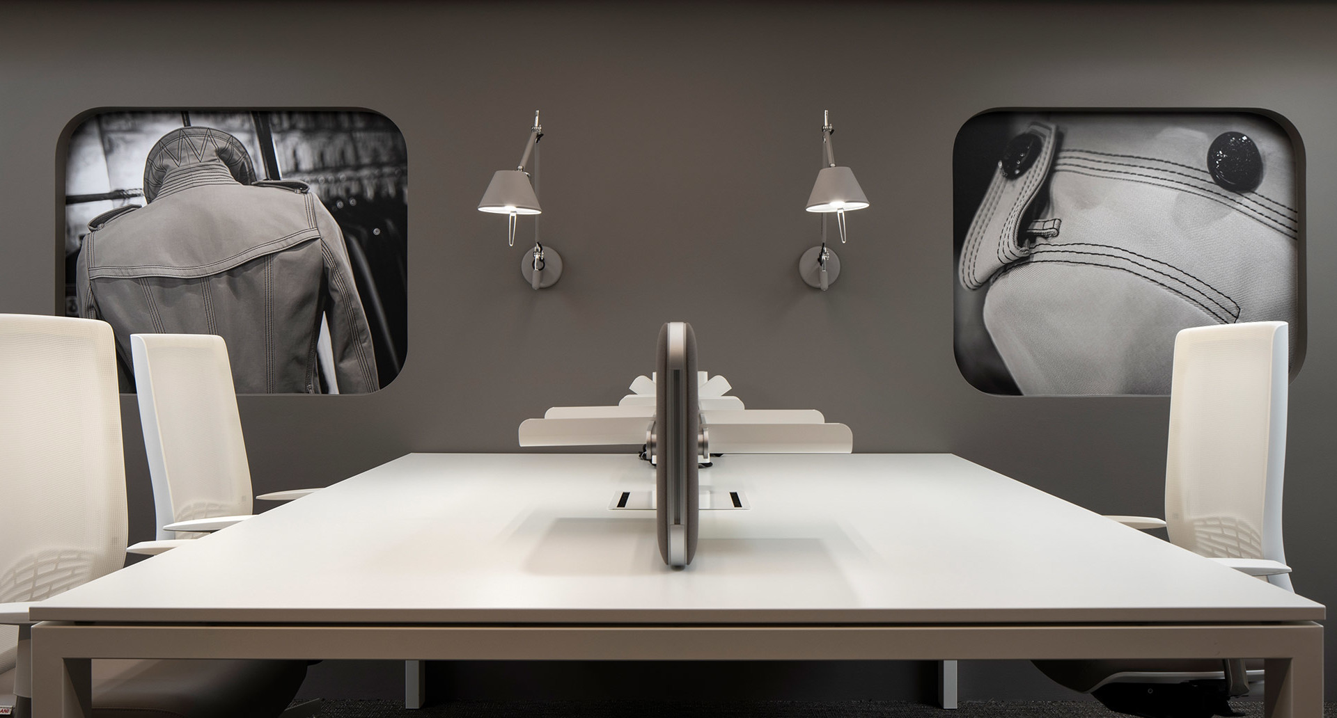 Postazione ufficio moderna con scrivania e sedie bianche, affiancata da due lampade da parete Artemide Tolomeo in alluminio spazzolato.