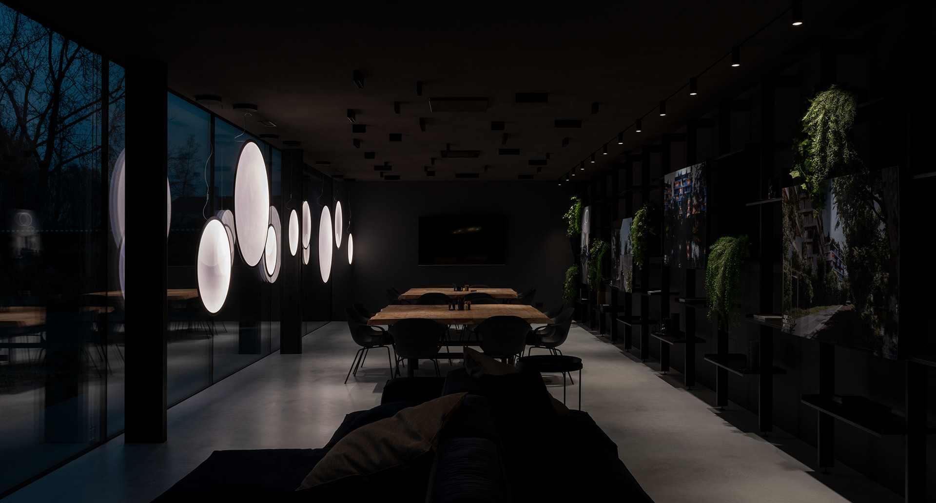 Sala da pranzo moderna e scura con lampade a sospensione circolari luminose, tavolo in legno, sedie nere e pareti verdi.