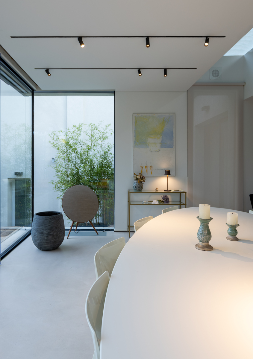 Sala da pranzo moderna con tavolo ovale bianco, faretti su binario a soffitto, vetrata a tutta altezza che si apre su un giardino interno