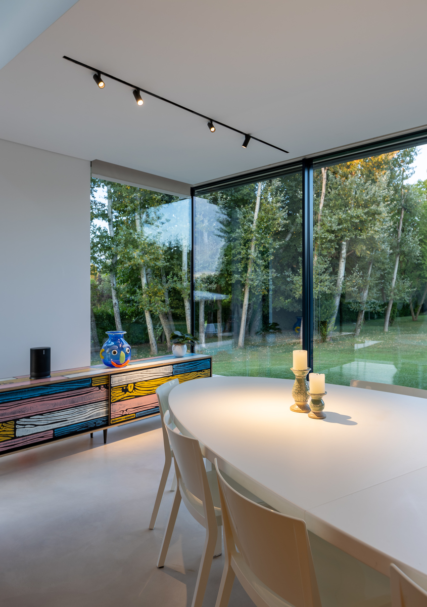 Sala da pranzo con tavolo rotondo bianco, faretti su binario Artemide a soffitto, finestre a tutta altezza con vista sul giardino