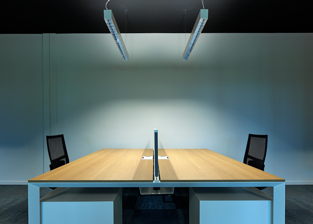 Two Artemide pendant linear lights illuminate a shared office workstation with two wooden desks and mesh chairs.