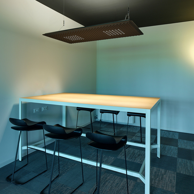 Artemide pendant lamp with perforated dark panel illuminating a high white table with four black stools in a modern workspace