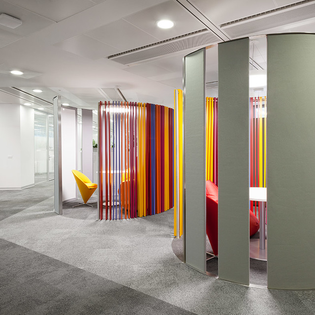 Interno di ufficio moderno con divisori a barre verticali colorate che creano pod curvi, luci a soffitto incassate e aree seduta vivaci