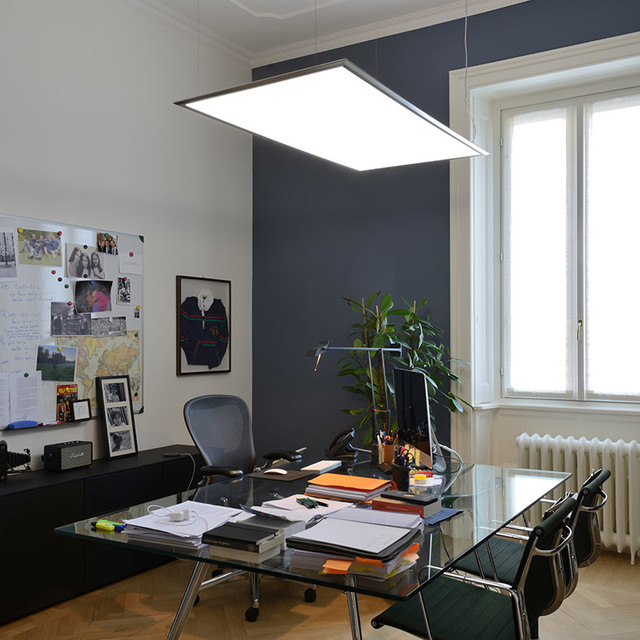 Artemide rectangular LED pendant lamp with slim dark frame, suspended over a glass office desk in a modern workspace.