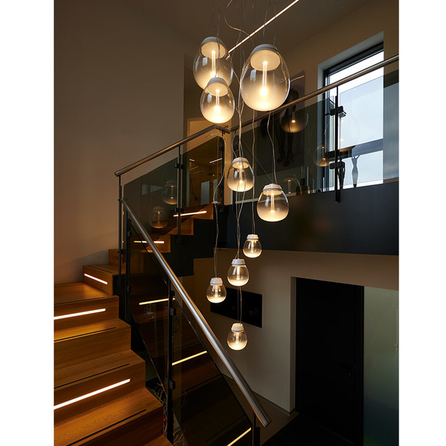 Più lampade a sospensione Artemide con diffusori in vetro ovale scendono a cascata su una scala moderna, creando una calda illuminazione su due piani.