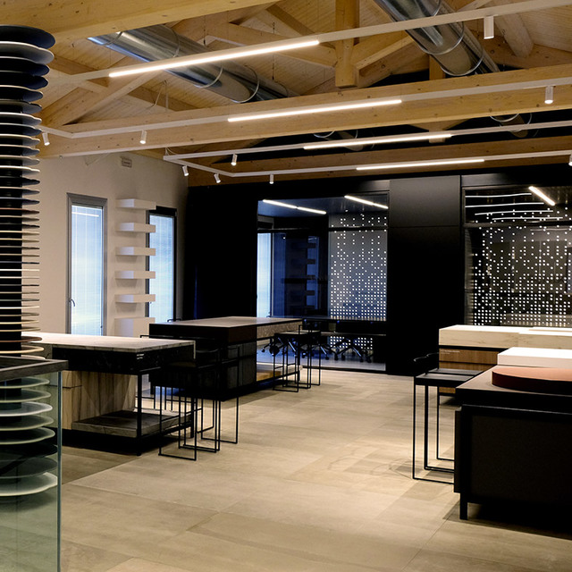 Modern showroom with Artemide linear ceiling lights, track spotlights on wooden beams, and illuminated display panels on dark walls.
