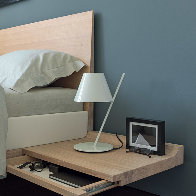 Lampada da tavolo Artemide bianca con stelo inclinato e paralume conico su comodino in legno in una camera da letto moderna
