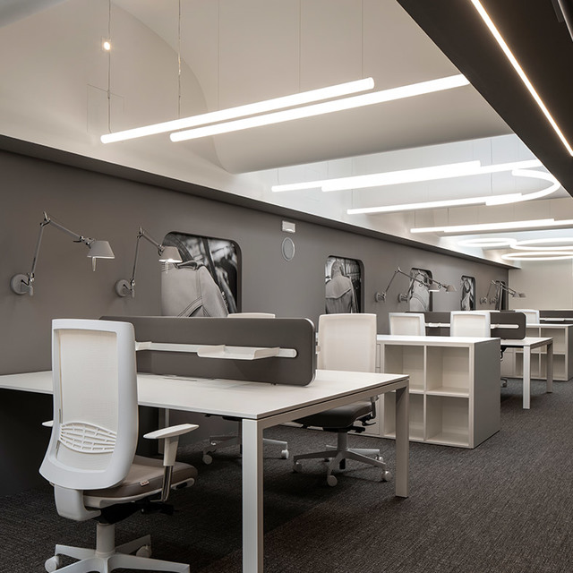 Ufficio moderno con lampade da parete Artemide Tolomeo e luci a sospensione LED lineari che illuminano postazioni bianche con sedie ergonomiche