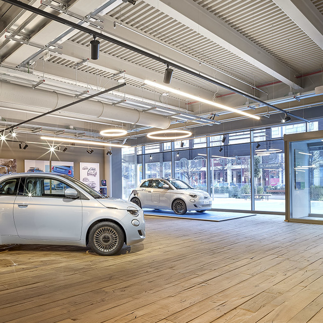 Fiat 500 electric car showroom lit by Artemide circular pendant lights and linear fixtures on an industrial ceiling.