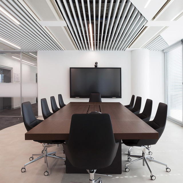 Sala conferenze moderna con tavolo in legno scuro, sedie nere, schermo a parete e sistema di illuminazione lineare a soffitto.
