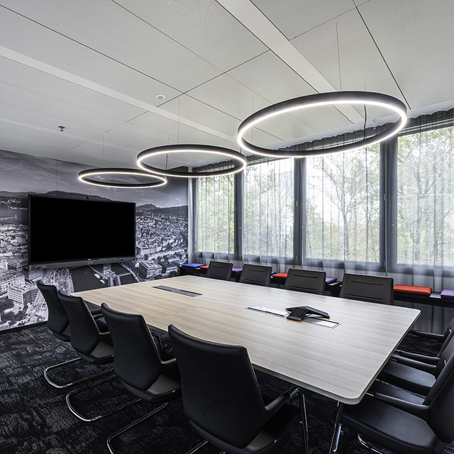 Conference room with three black circular LED pendant lights illuminating a long wooden table surrounded by black chairs.