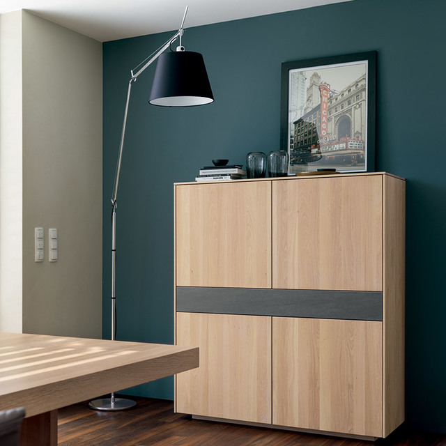 Lampada da terra Artemide Tolomeo Mega con paralume nero su braccio regolabile, accanto a un mobile in legno su parete verde petrolio.