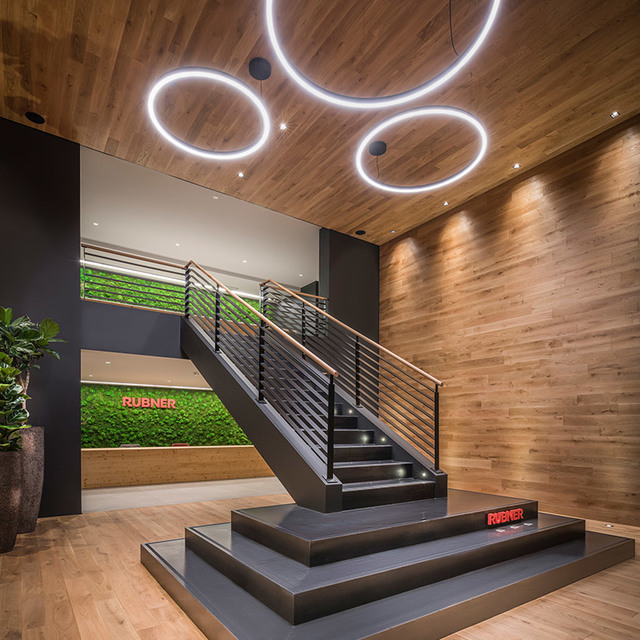 Ingresso showroom Rubner con lampade a sospensione circolari LED su soffitto in legno, scala e parete di muschio verde.