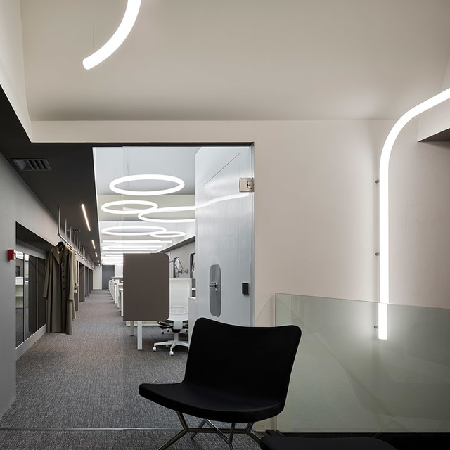 Ufficio moderno con strisce LED curve Artemide su soffitto e pareti, più anelli a sospensione circolari che illuminano uno spazio di lavoro aperto.
