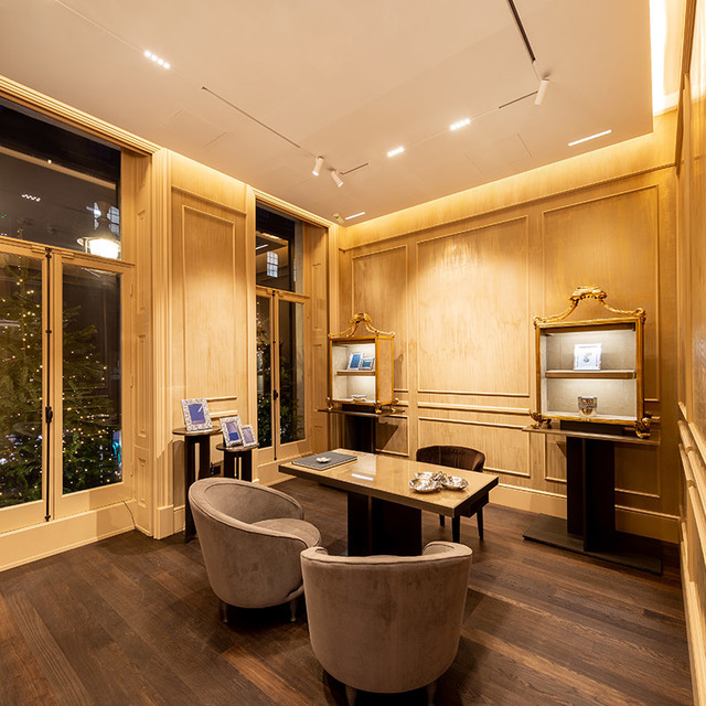 Elegant retail interior with warm recessed and track lighting illuminating wood-paneled walls, display cabinets, and a central meeting table with chairs.
