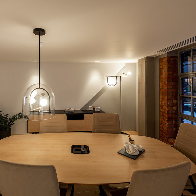 Dining room with oval wooden table, dome-shaped glass pendant lamp and arc floor lamp casting warm light on chairs and sideboard.