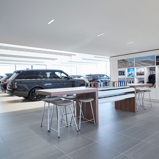 Car showroom interior with Artemide recessed linear ceiling lights illuminating display tables, stools, and luxury SUVs on the floor.