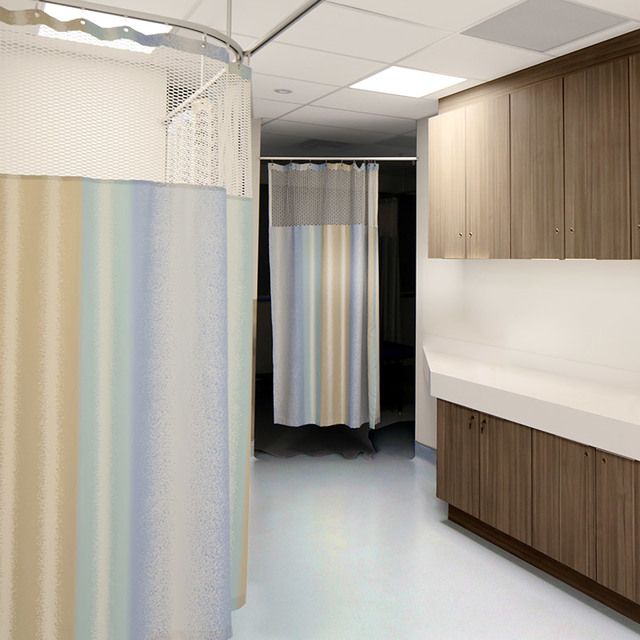 Corridoio di stanza ospedaliera con tende divisorie su binari a soffitto, armadi con finitura in legno e pannelli luminosi a soffitto incassati.