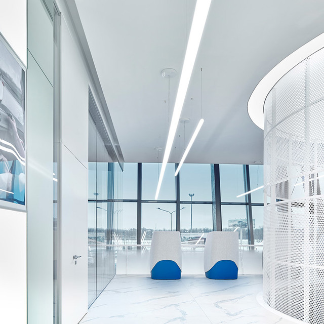 Ingresso ufficio moderno con lampade lineari a sospensione Artemide su soffitto bianco, pareti in vetro e due sedie bianche con sedute blu.