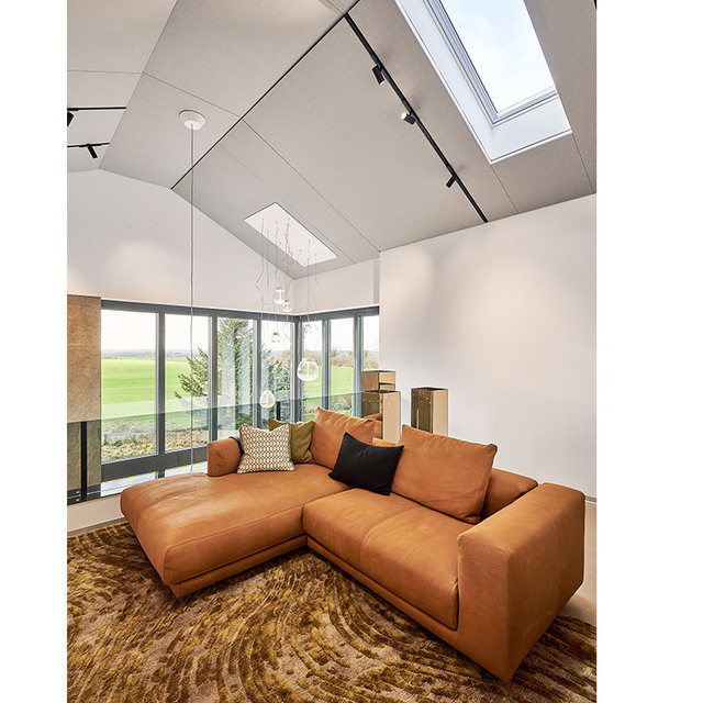 Soggiorno moderno con soffitto a volta, faretti su binario, sospensioni a globo in vetro, lucernari, divano angolare in pelle cognac e finestre a tutta altezza.