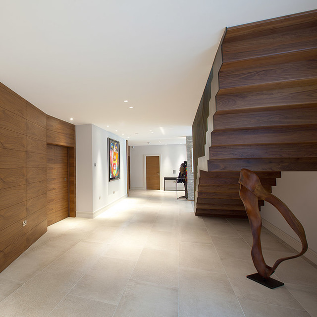 Modern hallway with recessed ceiling lights, wooden staircase, curved wall panels, colorful artwork, and a bronze sculpture on marble floor