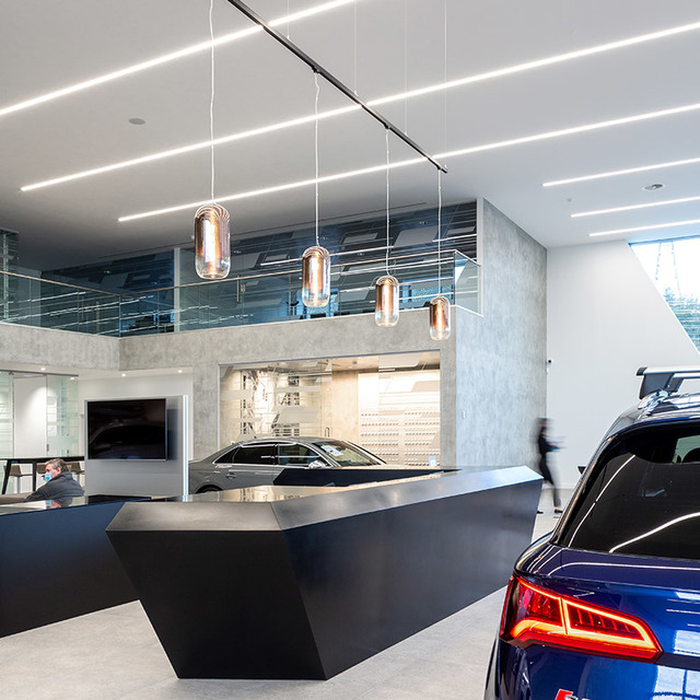 Showroom auto con lampade a sospensione Artemide Nula in vetro ambrato sopra una reception angolare scura, con luci lineari a soffitto.