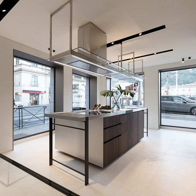 Showroom cucina moderna con isola centrale, cassetti in legno scuro, cappa in acciaio e faretti da incasso Artemide su binari a soffitto.