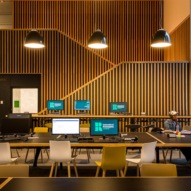 University of Roehampton London computer lab with three black pendant lamps illuminating workstations against a wooden slat wall.