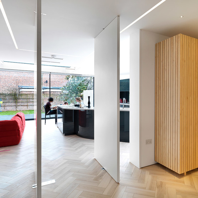 Cucina open space moderna con luci a soffitto lineari LED da incasso Artemide, pavimento in legno a spina di pesce, parete in vetro e vista giardino.