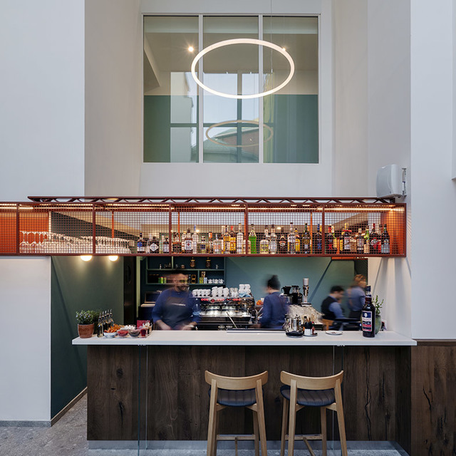 Bar interior with Artemide circular pendant light above counter, staff working behind bar with liquor bottles on shelved display