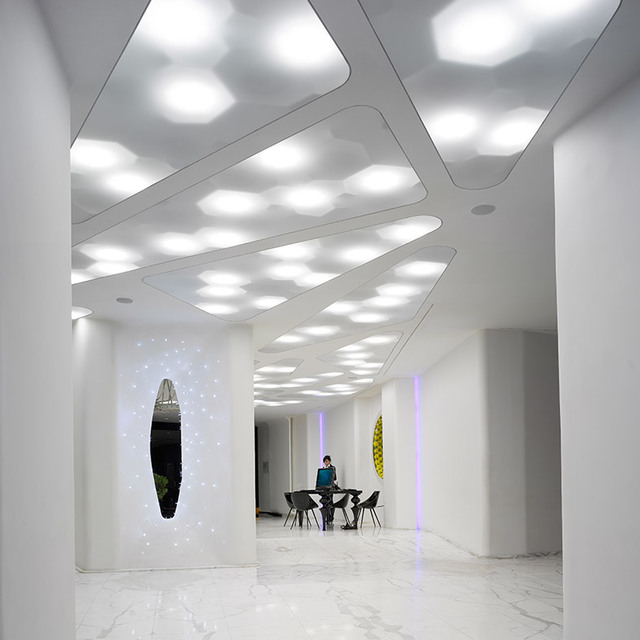 Interno bianco moderno con pannelli a soffitto di forma organica con luci incassate, che creano un corridoio luminoso con pavimento in marmo.