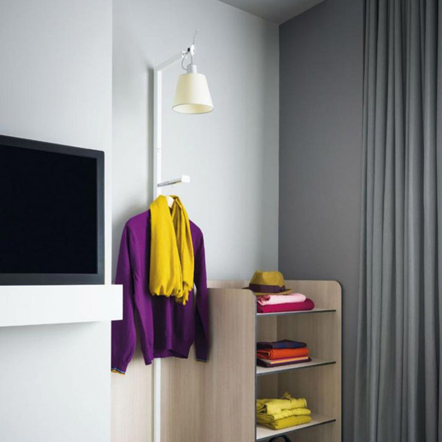 Lampada da parete Artemide Tolomeo con paralume crema montata in un'area guardaroba con abiti colorati piegati su scaffali in legno