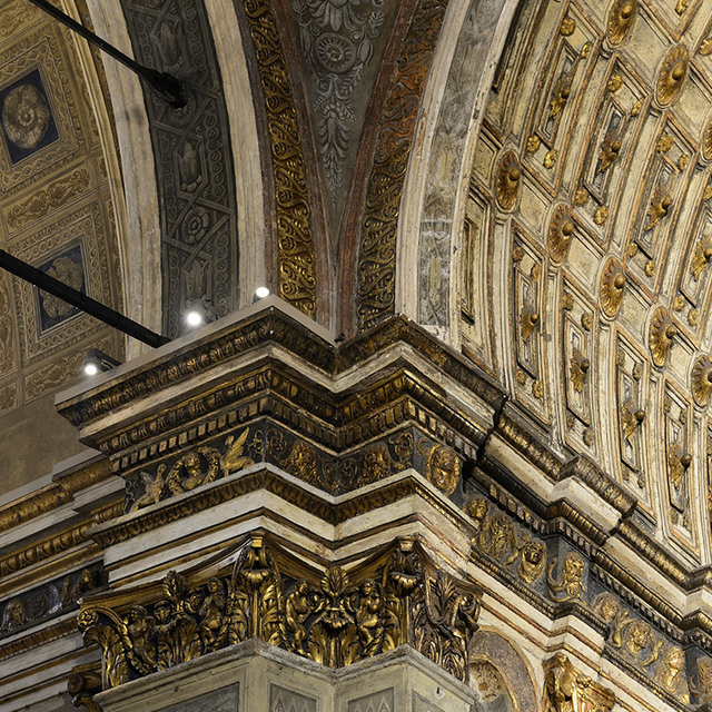 Ornate baroque ceiling with gilded cornices and carved capitals, illuminated by Artemide spotlights mounted on a track system