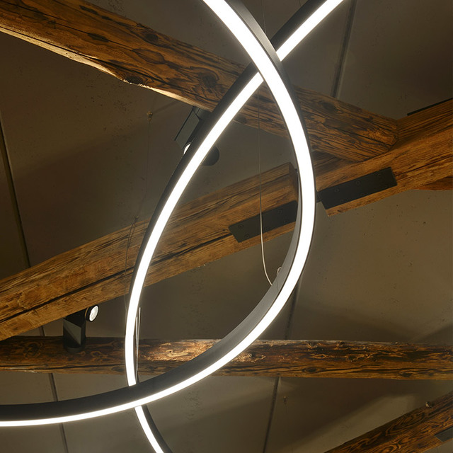 Lampada a sospensione Artemide ad anello LED circolare in nero, che emette luce bianca intensa, installata tra travi rustiche in legno