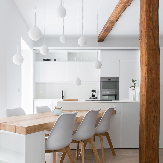 Cucina bianca moderna con tavolo da pranzo in legno, sedie scandinave e multiple lampade a sospensione sferiche bianche appese al soffitto