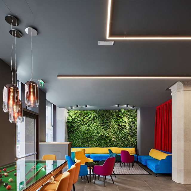Lounge with Artemide glass pendant lights, linear ceiling LEDs, colorful sofas, green living wall, and a billiard table in foreground