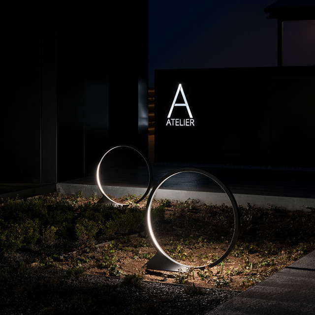 Due lampade da terra LED circolari Artemide con anelli luminosi illuminano un giardino di notte davanti a un edificio Atelier