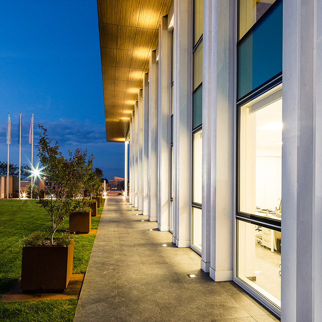 Esterno di edificio moderno al crepuscolo con faretti Artemide da incasso a pavimento che illuminano colonne bianche lungo una facciata vetrata.