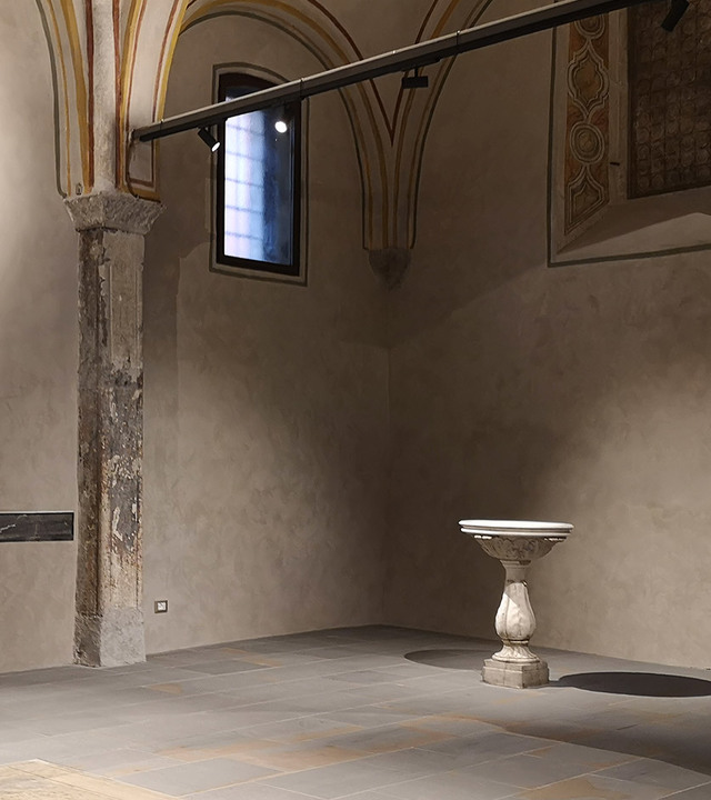Interno storico con volta affrescata e faretti su binario Artemide che illuminano una colonna in pietra e una vasca su piedistallo in marmo antico.