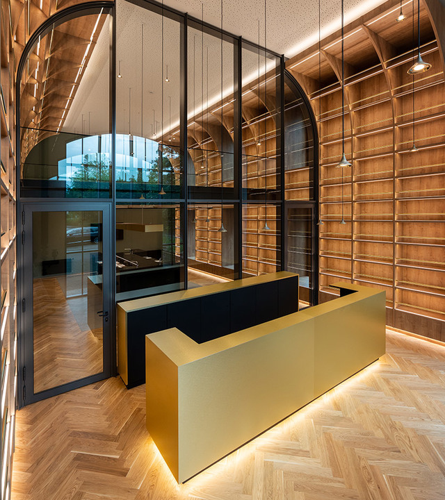 Area reception moderna con scrivania dorata, pavimento in legno a spina di pesce, pareti arcuate rivestite in legno e illuminazione LED lineare a soffitto