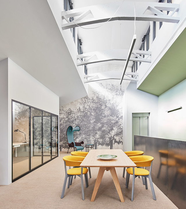 Modern meeting room with wooden table, yellow chairs, tree mural, and sculptural white ceiling installation with pendant lighting.