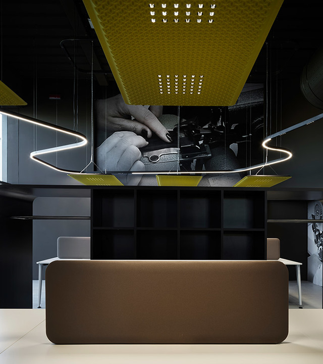 Modern interior with Artemide circular LED pendant lights suspended over a reception desk, with yellow acoustic ceiling panels above.