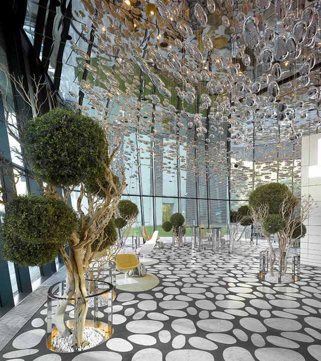 Atrio lussuoso con installazione a soffitto di bolle di vetro scultoree, alberi topiaria curati, pavimento a motivo di ciottoli e sedute moderne.