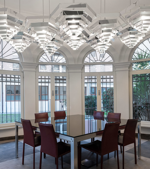 Elegant dining room with a square table and red leather chairs beneath large Artemide modular pendant lights with layered reflectors.