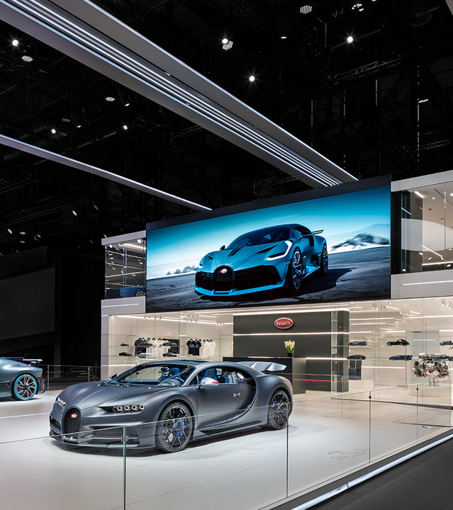 Showroom Bugatti con una supercar grigio scuro in esposizione, illuminata da lampade lineari a soffitto e faretti da incasso Artemide.